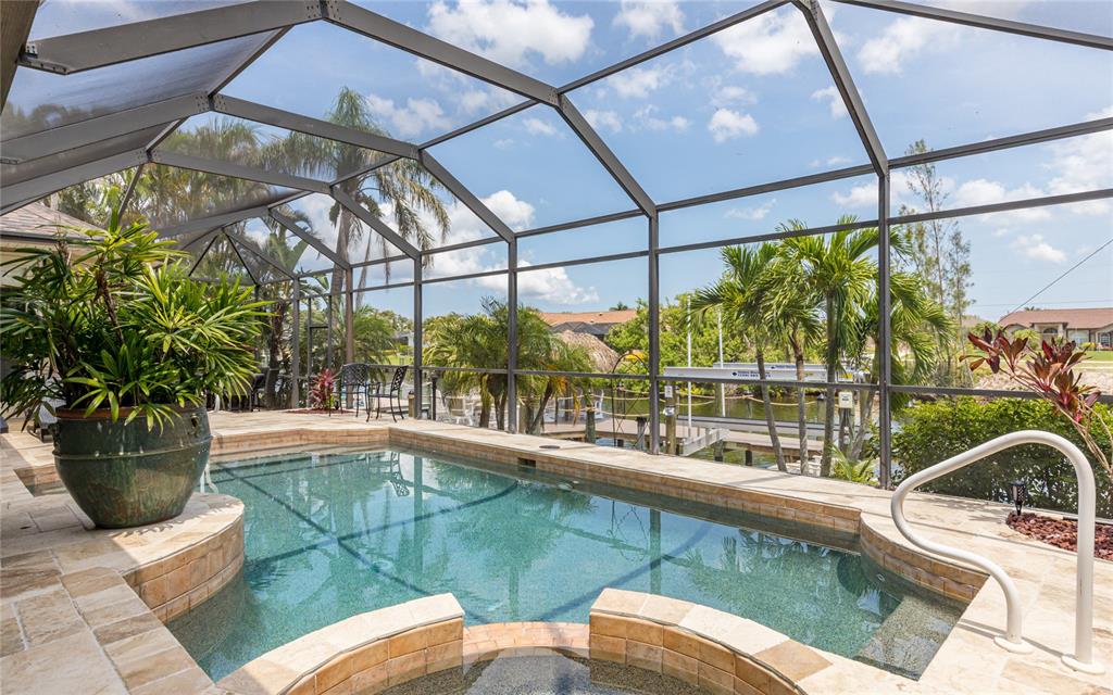A screened-in pool and spa area with stone decking overlooking a canal and boat dock — 2317 SW 43RD LANE, CAPE CORAL, FL