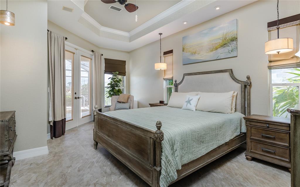 A bedroom features a king bed, tray ceiling, tile flooring, and glass doors to a patio — 2317 SW 43RD LANE, CAPE CORAL, FL
