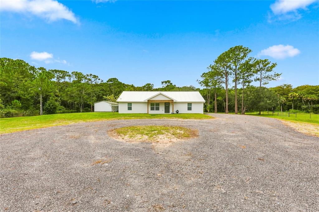 A white single-story house with a metal roof sits behind a large gravel driveway — 1315 NE 342ND TRAIL, OKEECHOBEE, FL
