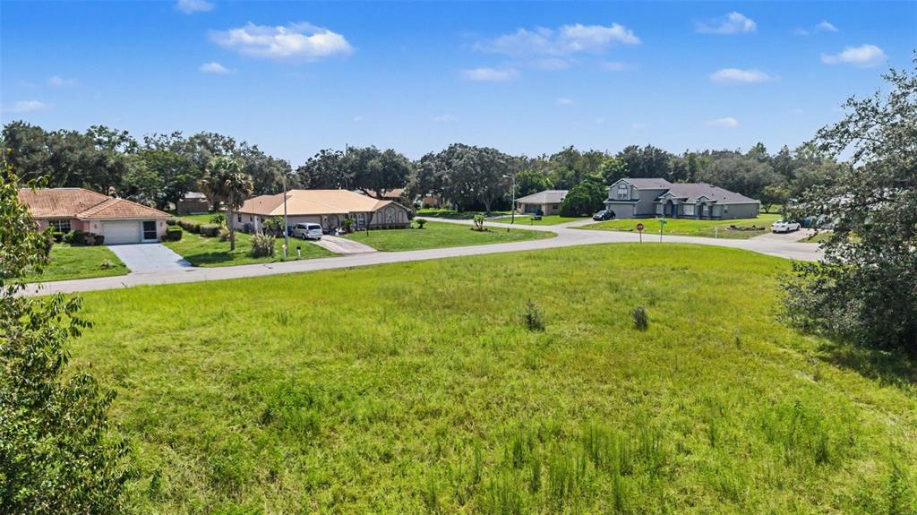 A large, grassy vacant lot sits in the foreground of a suburban residential street — NORTHWIND COURT, SPRING HILL, FL
