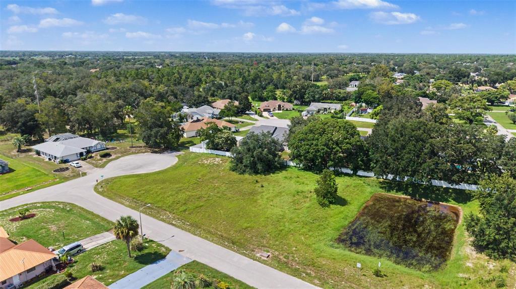 An aerial view shows a vacant grassy lot with a small pond in a residential neighborhood — NORTHWIND COURT, SPRING HILL, FL