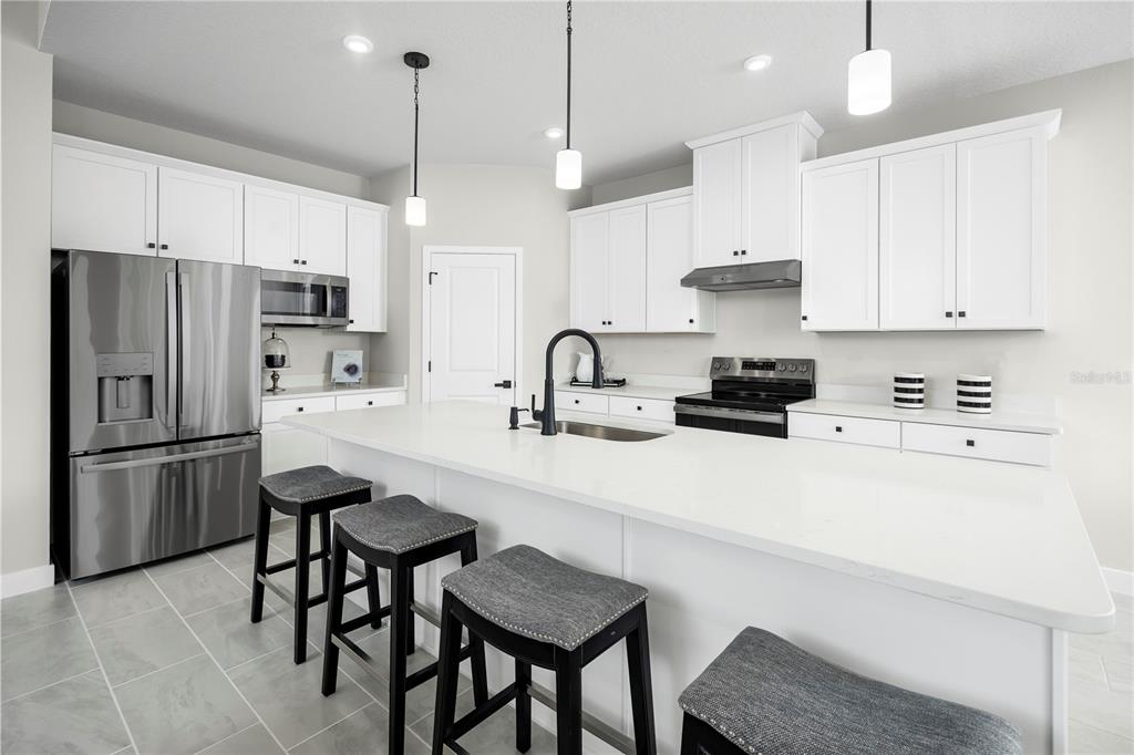A modern kitchen features white cabinets, stainless steel appliances, a large island, and gray stools — 14413 WOODLAND PRESERVE TRAIL, PARRISH, FL