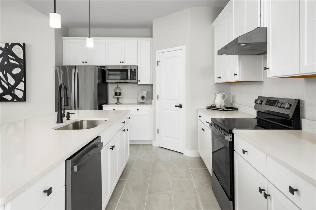 A modern kitchen features white cabinets, stainless steel appliances, a quartz island, and tile flooring — 14413 WOODLAND PRESERVE TRAIL, PARRISH, FL