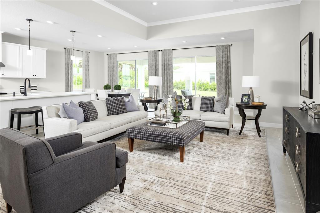 A bright, open-concept living room features two sofas, a plaid ottoman, and a dark sideboard — 14413 WOODLAND PRESERVE TRAIL, PARRISH, FL