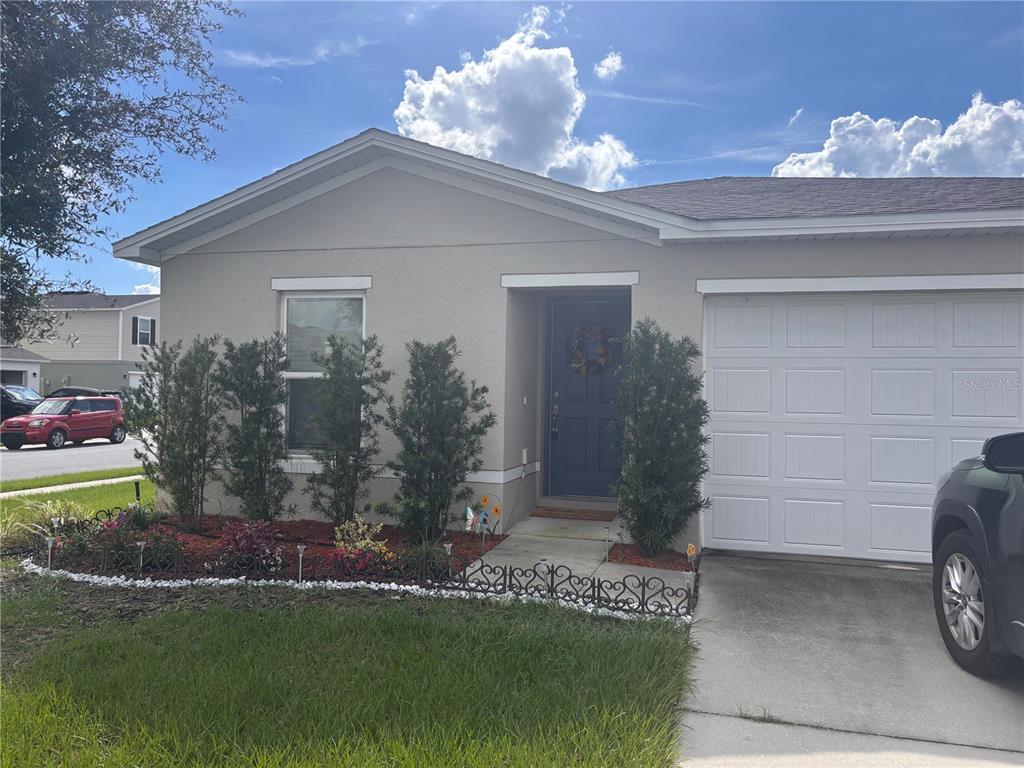 A blue front door is centered between two tall evergreen shrubs and a white garage — 1876 IOWA DRIVE, SUMTERVILLE, FL