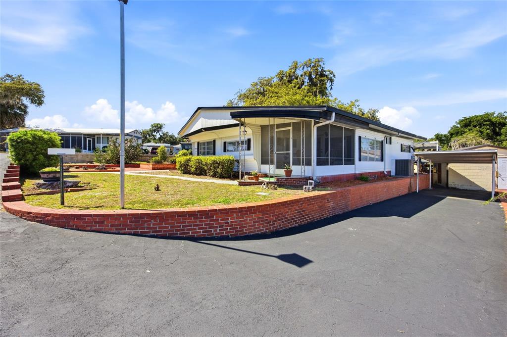 A white mobile home features a brick patio, a birdbath, and a large oak tree — 3896 PICCIOLA ROAD UNIT 411, FRUITLAND PARK, FL