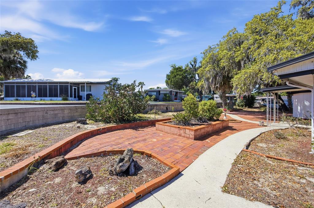 A white mobile home with a brick patio, a birdbath, and a large oak tree — 3896 PICCIOLA ROAD UNIT 411, FRUITLAND PARK, FL