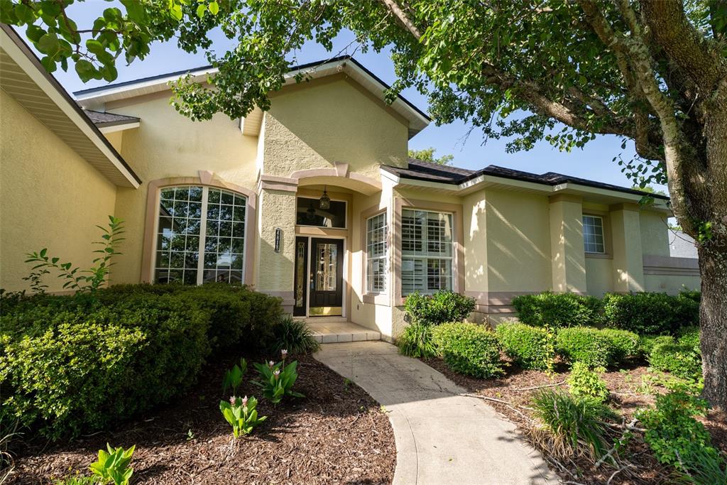 A beige stucco house with a front walkway, arched window, and landscaped garden beds — 4818 SE 11TH PLACE, OCALA, FL