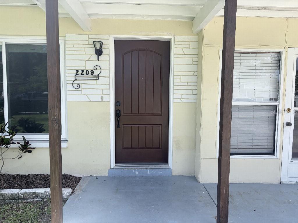 The exterior of a house features a brown front door, address numbers, and porch posts — 2209 EUCLID CIRCLE S, CLEARWATER, FL