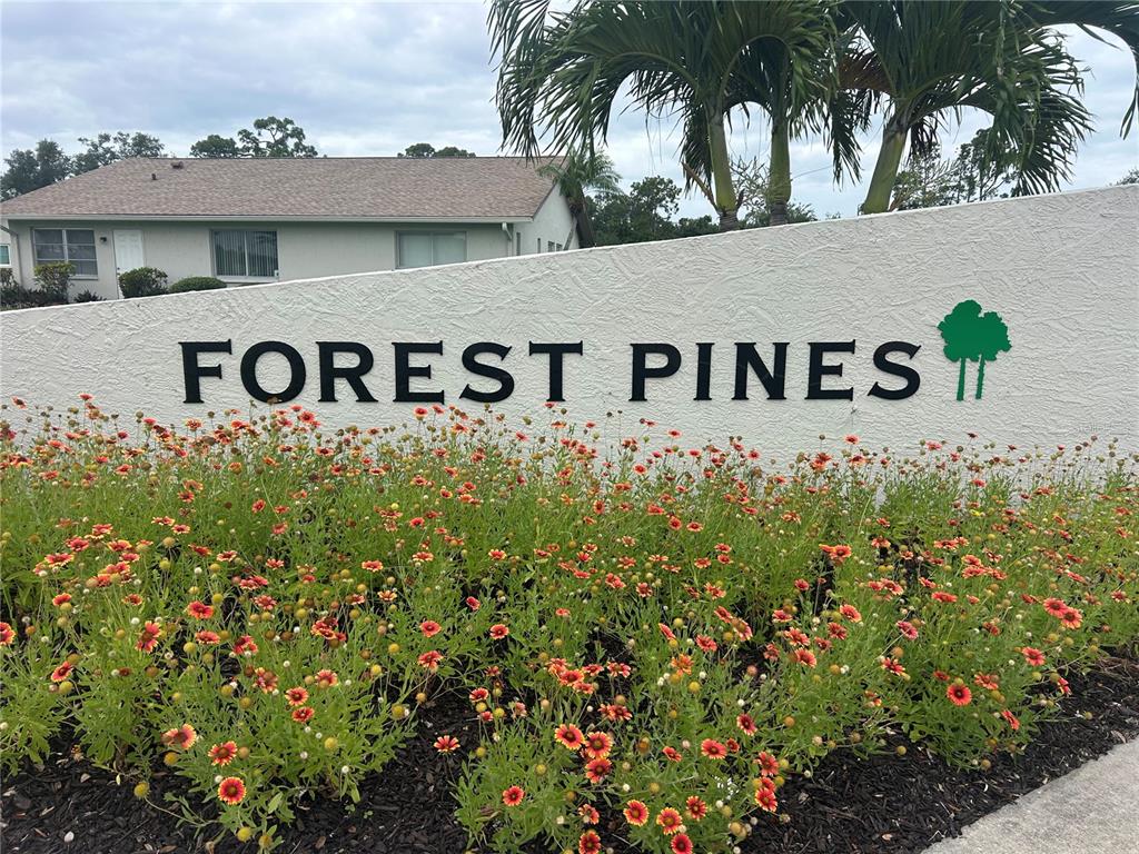 A white wall with the text Forest Pines sits behind a bed of colorful flowers — 1548 GRAND BOULEVARD UNIT 109, SARASOTA, FL