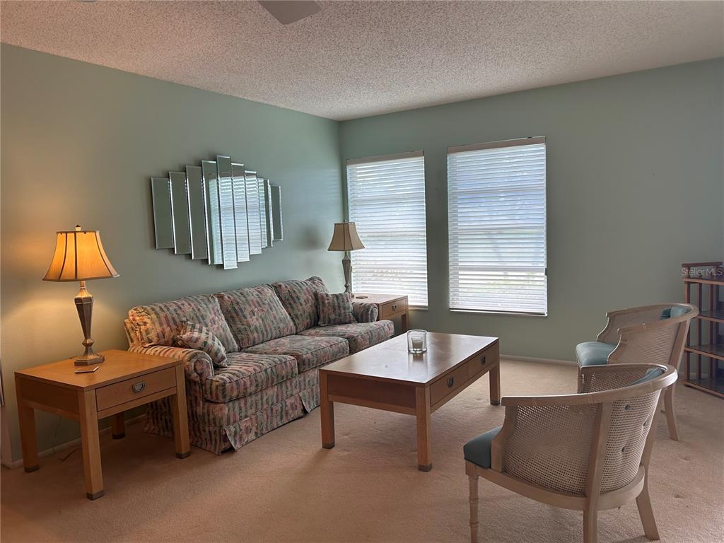 A living room features a floral sofa, wooden coffee table, two armchairs, and a wall mirror — 1548 GRAND BOULEVARD UNIT 109, SARASOTA, FL