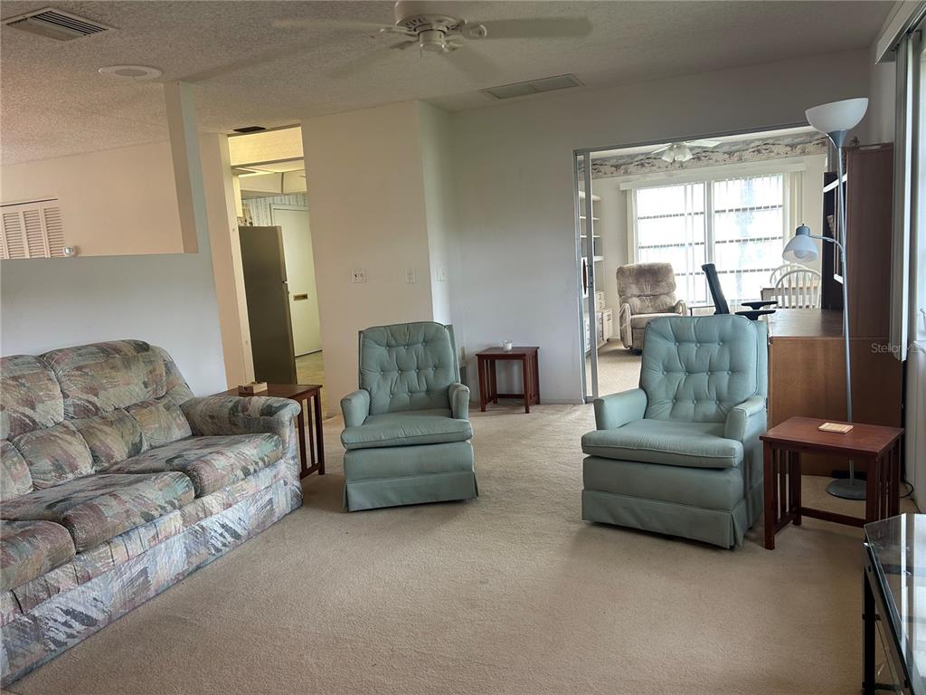 A living room features a patterned sofa, two light blue armchairs, and beige carpeting — 1548 GRAND BOULEVARD UNIT 109, SARASOTA, FL