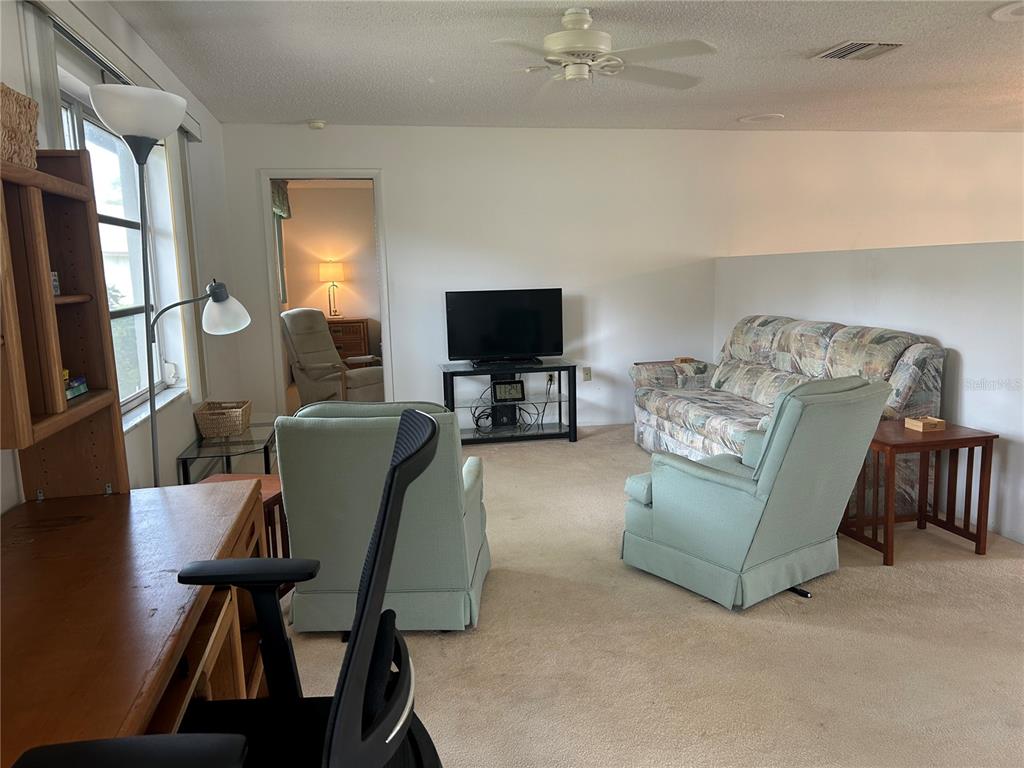A living room features a patterned sofa, two light green armchairs, and a television stand — 1548 GRAND BOULEVARD UNIT 109, SARASOTA, FL