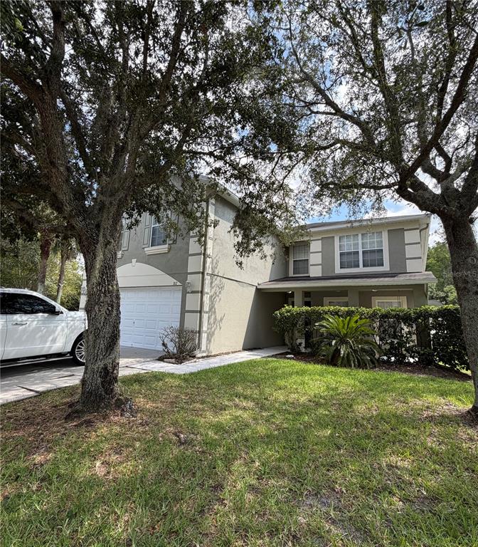 A two-story house with a white garage, gray stucco siding, and large trees in front — 312 WINDROSE DRIVE, ORLANDO, FL