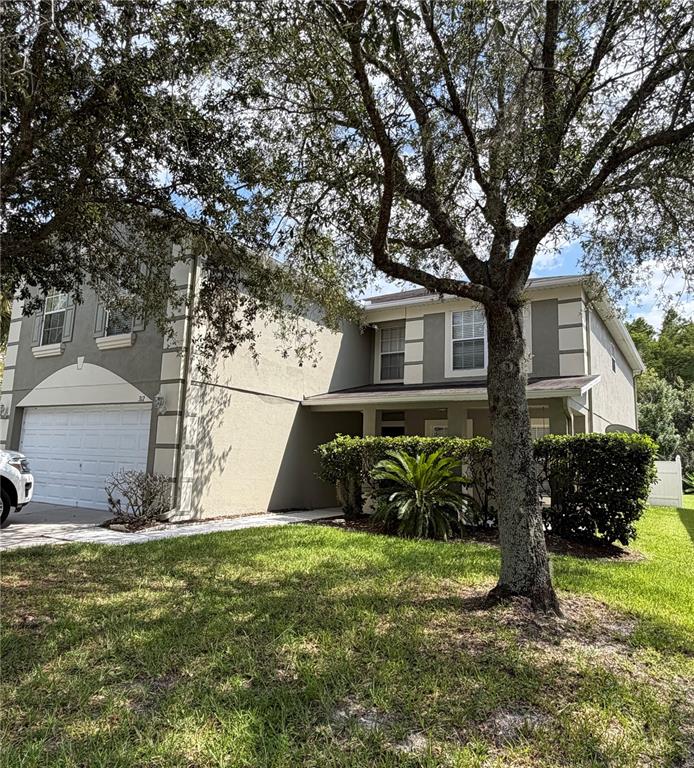 A two-story house with a garage, light-colored stucco exterior, and a large tree in front — 312 WINDROSE DRIVE, ORLANDO, FL