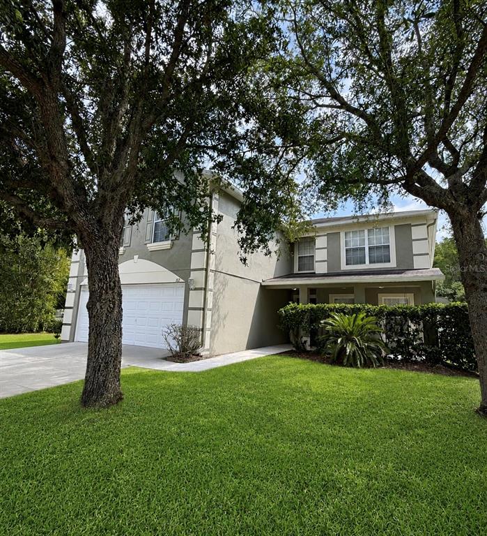 A two-story house with a two-car garage, light-colored stucco exterior, and mature trees in front — 312 WINDROSE DRIVE, ORLANDO, FL