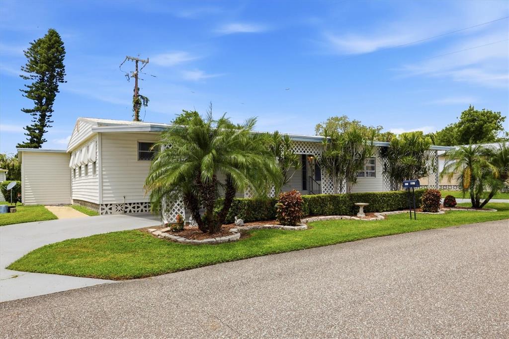 A single-story manufactured home with light siding, a palm tree, and a manicured hedge — 1407 41ST AVENUE E, ELLENTON, FL