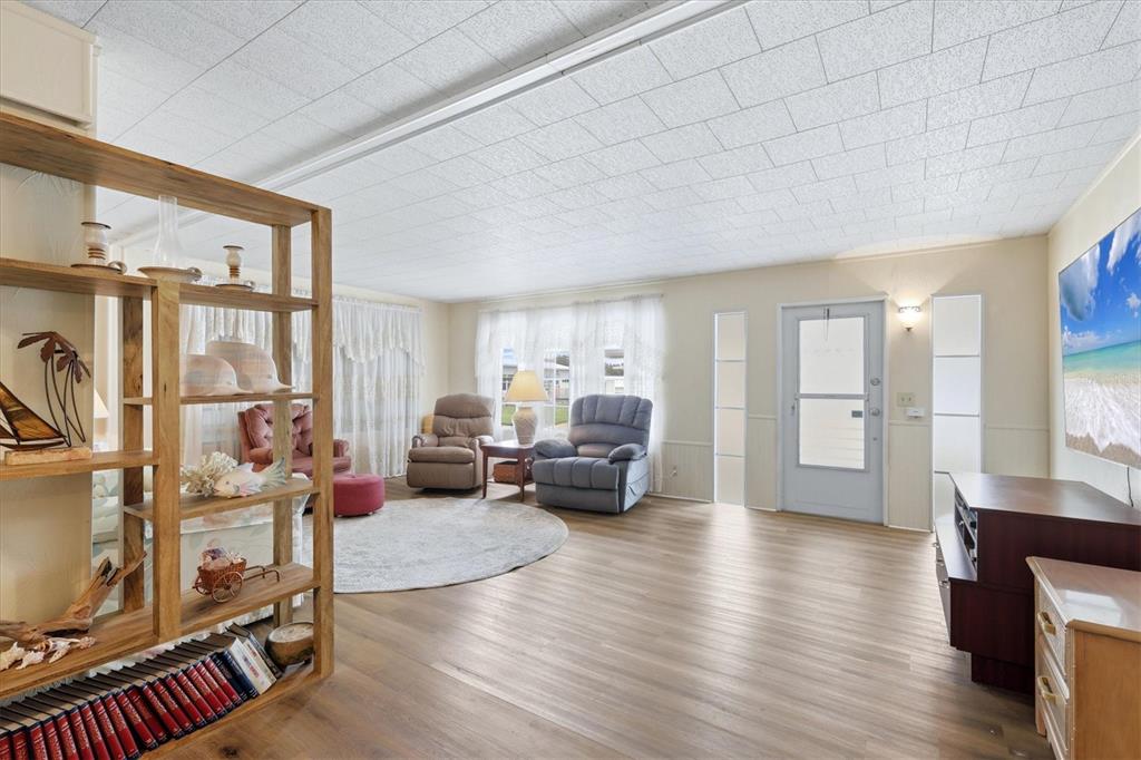 A living room features light wood-look flooring, a drop ceiling, and a wooden shelving unit — 1407 41ST AVENUE E, ELLENTON, FL