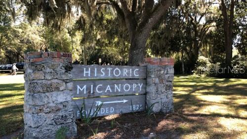 A stone and brick sign reads Historic Micanopy Founded 1821 beneath large, moss-draped oak trees — 302 NE BAY AVENUE, MICANOPY, FL