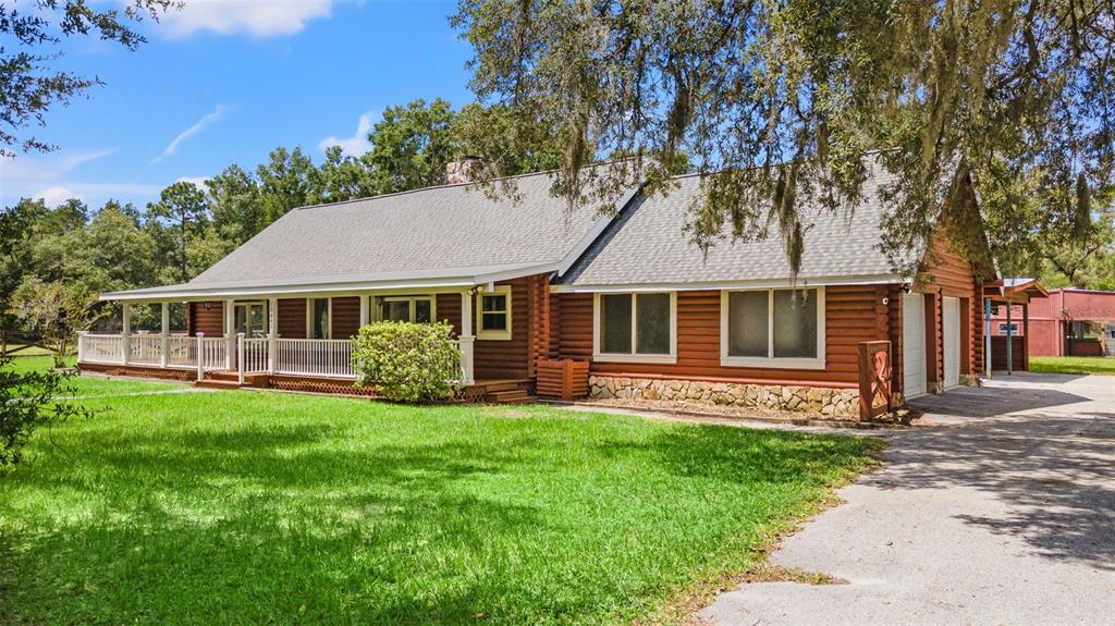 A single-story log cabin home features a long front porch, stone foundation, and attached garage — 18441 OAKLAWN DRIVE, SPRING HILL, FL