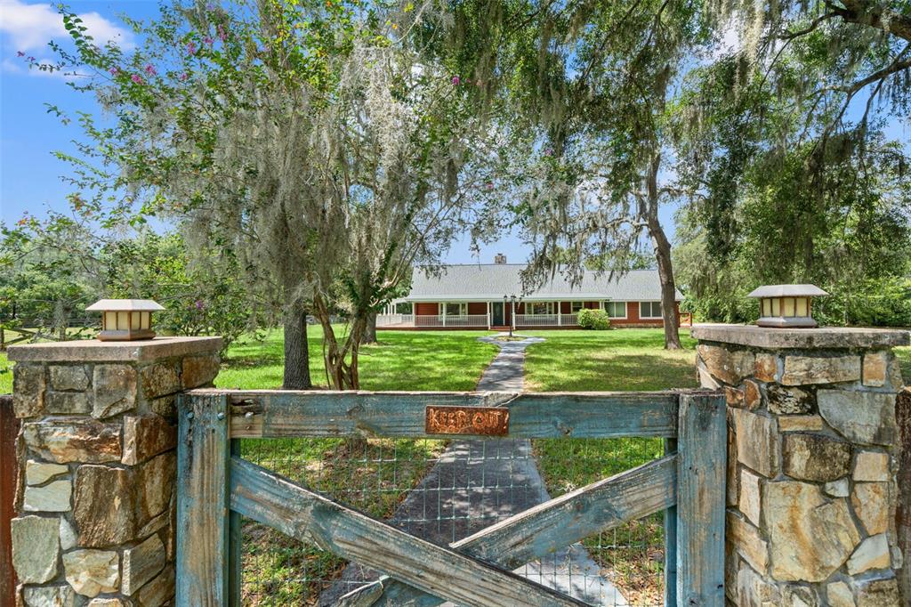 A rustic wooden gate with a keep out sign leads to a house with trees — 18441 OAKLAWN DRIVE, SPRING HILL, FL