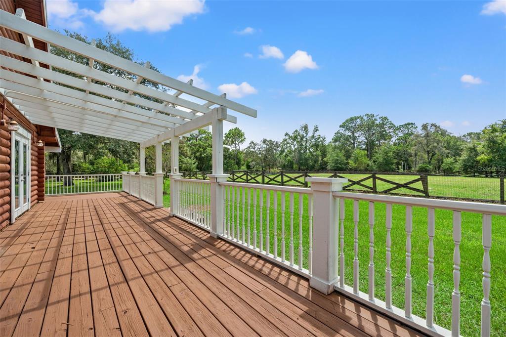 A wooden deck with a white pergola and railing overlooks a grassy backyard and fence — 18441 OAKLAWN DRIVE, SPRING HILL, FL
