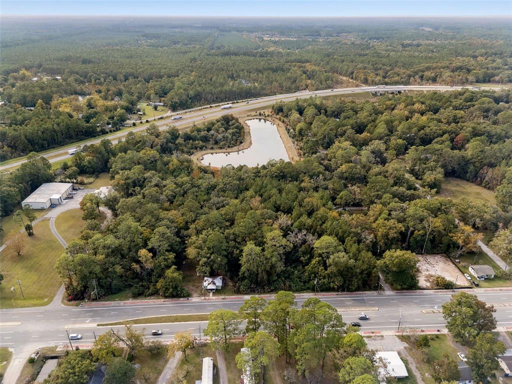 An aerial view shows a wooded lot with a pond, a house, and nearby highways — 660 US HIGHWAY 301 S, BALDWIN, FL