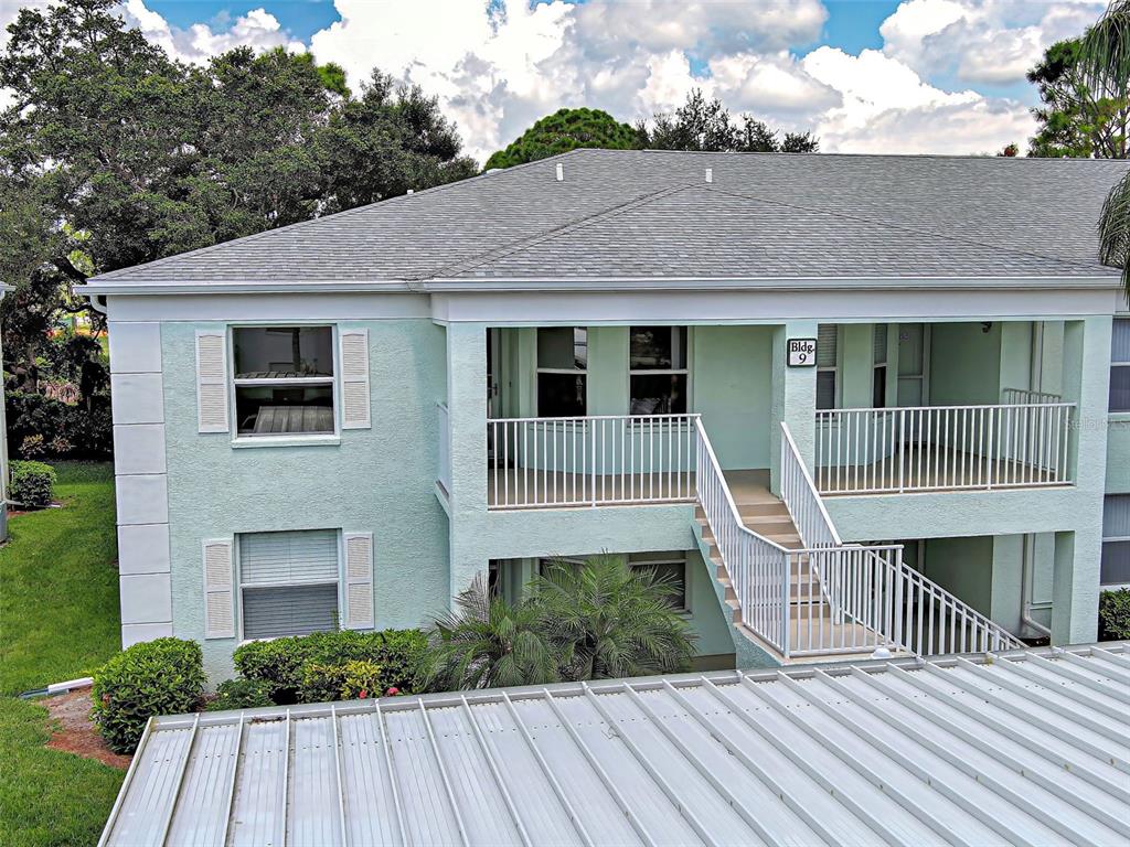 A two-story light green apartment building exterior features a white staircase and a metal roof — 5725 GREENWOOD AVENUE UNIT 9201, NORTH PORT, FL