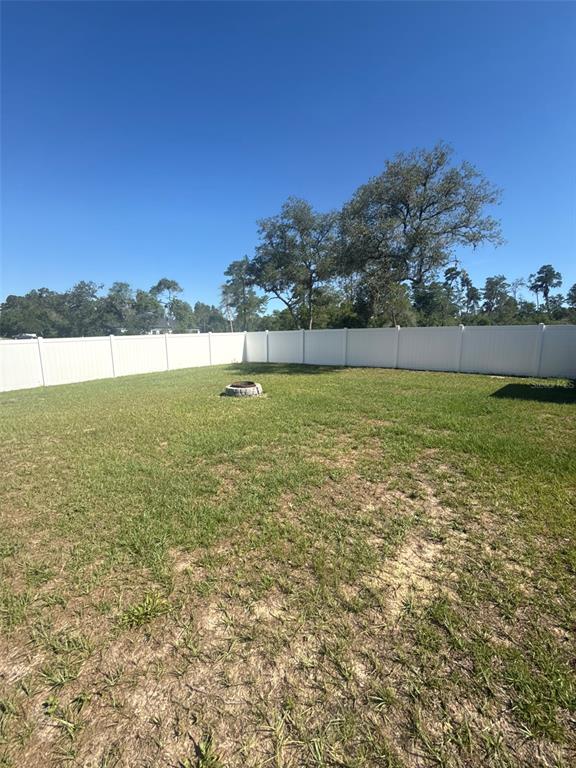 A grassy backyard features a stone fire pit and is enclosed by a white fence — 16292 SW 30 TERRACE UNIT 1, OCALA, FL