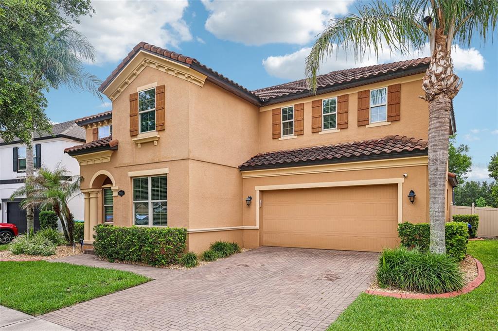 A two-story tan stucco house with a tile roof, brown shutters, and a paved driveway — 9117 OUTLOOK ROCK TRAIL, WINDERMERE, FL