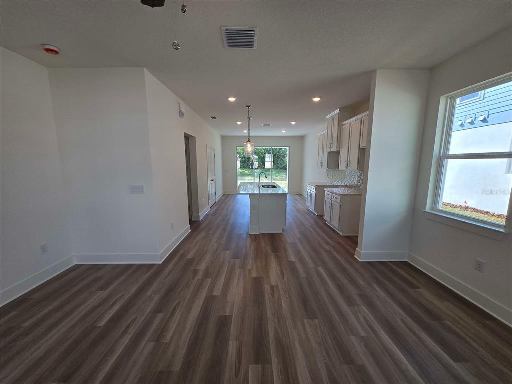 An open-concept kitchen and living area features white cabinets, a central island, and wood-look flooring — 3836 DAYBREAK RUN LOOP, SPRING HILL, FL