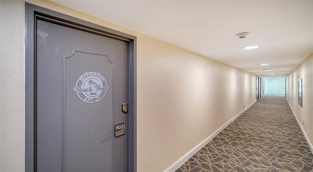 A gray door with a decorative decal leads into a long, carpeted apartment hallway — 4822 OCEAN BOULEVARD UNIT 2F, SARASOTA, FL