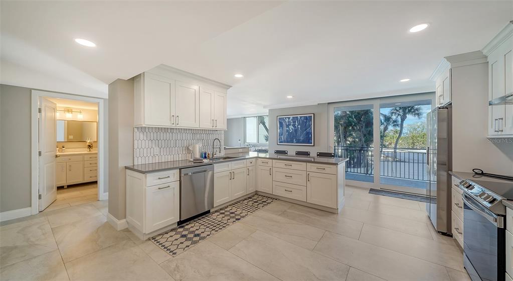 A modern kitchen with white cabinets, stainless steel appliances, and tile flooring opens to a balcony — 4822 OCEAN BOULEVARD UNIT 2F, SARASOTA, FL