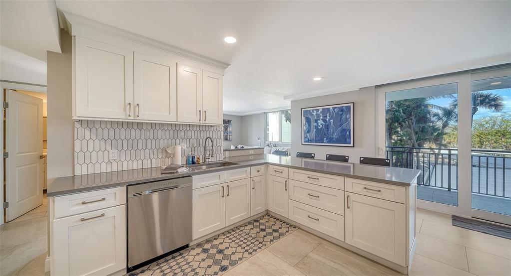 A kitchen with white cabinets, gray countertops, a tiled backsplash, and a sliding glass door — 4822 OCEAN BOULEVARD UNIT 2F, SARASOTA, FL