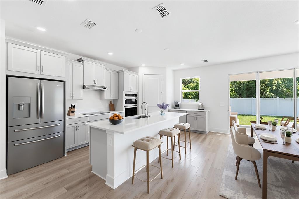 A modern kitchen features white cabinetry, stainless steel appliances, a center island, and wood flooring — 2321 HUANIER COURT, APOPKA, FL