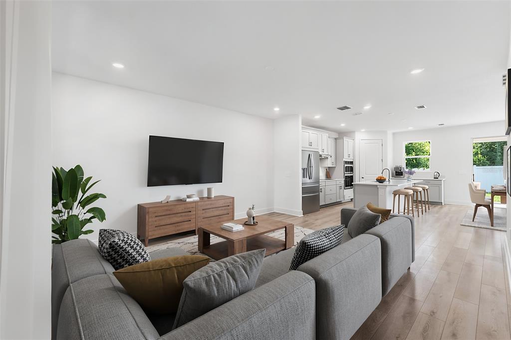 An open-concept living room and kitchen featuring gray sectional seating, wood furniture, and light flooring — 2321 HUANIER COURT, APOPKA, FL