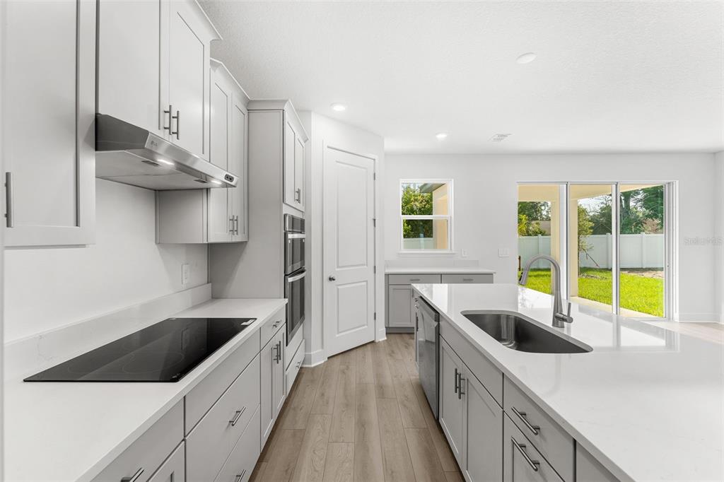 A modern kitchen features gray cabinetry, white countertops, stainless steel appliances, and wood-look flooring — 2321 HUANIER COURT, APOPKA, FL