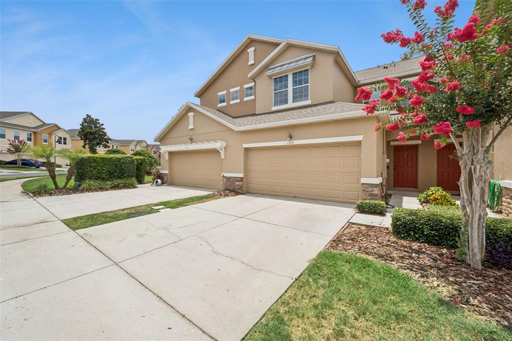 A two-story tan townhouse with two garage doors and a red front door — 1320 GLENLEIGH DRIVE, OCOEE, FL
