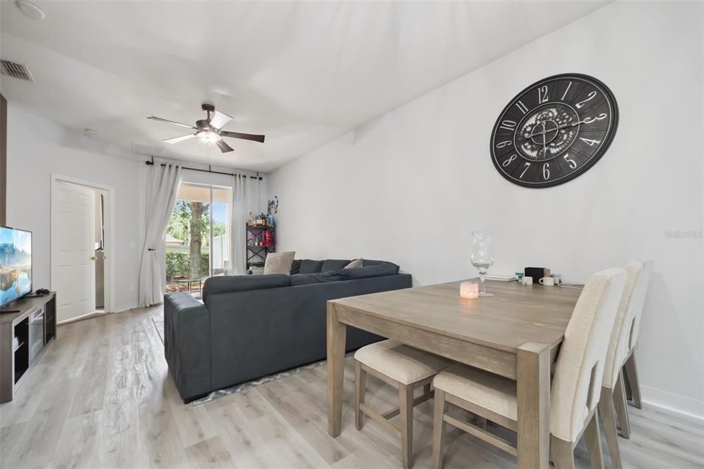 A living and dining area features light wood-look flooring, a gray sectional, and a wall clock — 1320 GLENLEIGH DRIVE, OCOEE, FL