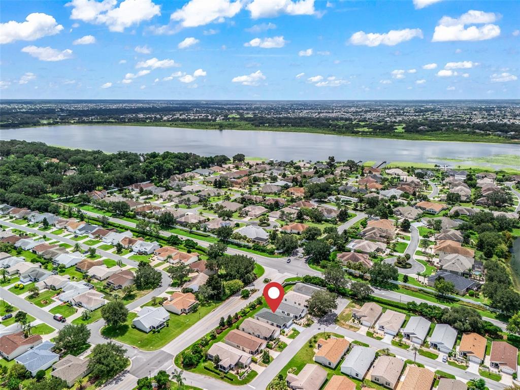An aerial view shows a suburban neighborhood with houses, streets, and a large lake nearby — 973 YORK TERRACE, THE VILLAGES, FL