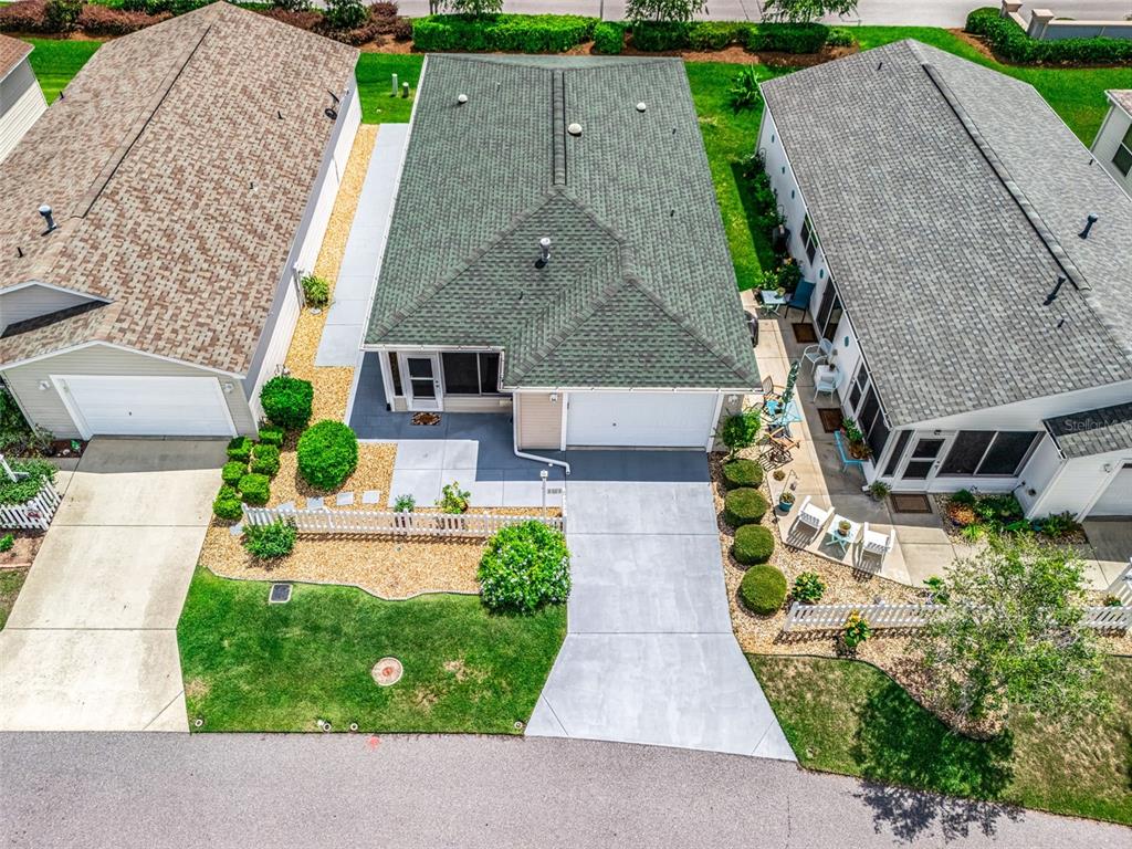 An aerial view shows three suburban houses with driveways, green roofs, and landscaped front yards — 973 YORK TERRACE, THE VILLAGES, FL