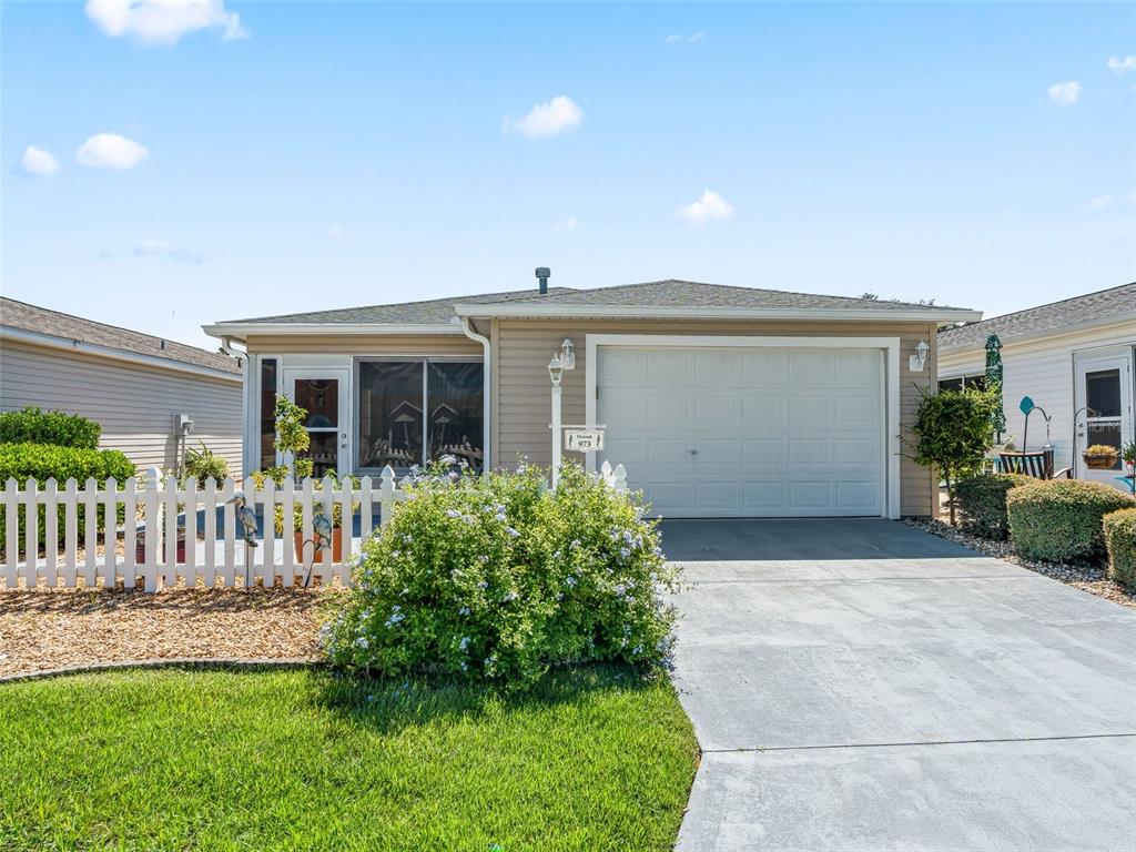 A single-story house with beige siding, a white garage door, and a white picket fence — 973 YORK TERRACE, THE VILLAGES, FL