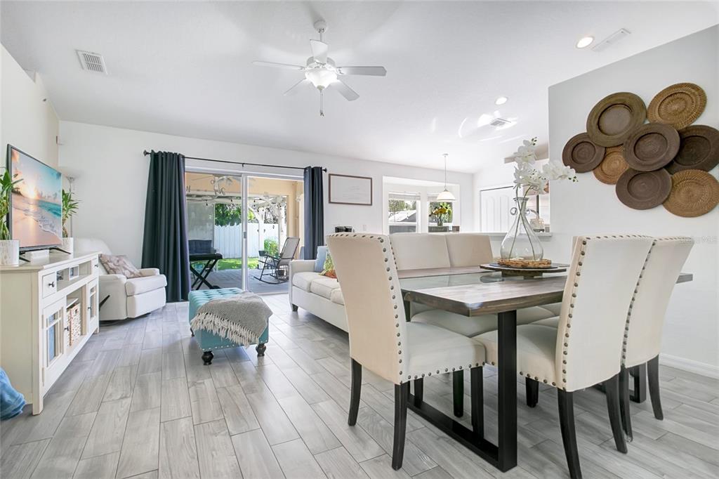 An open-concept living and dining area features light wood-look tile flooring and a sliding glass door — 4202 CRACKER COURT, ST CLOUD, FL