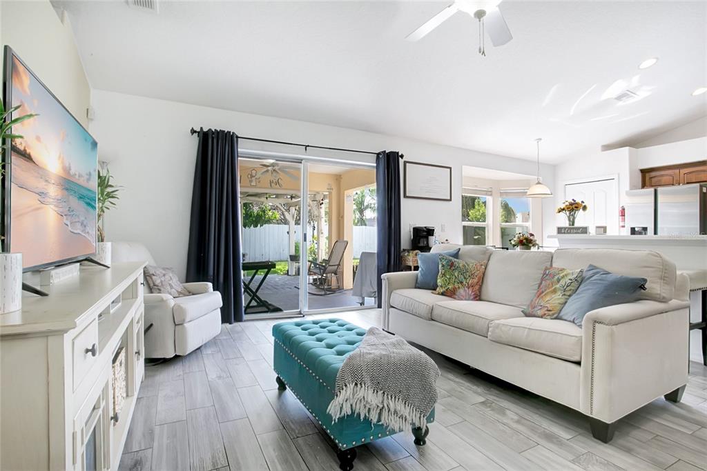 A living room features light wood-look tile floors, a white sofa, a teal ottoman, and sliding doors — 4202 CRACKER COURT, ST CLOUD, FL