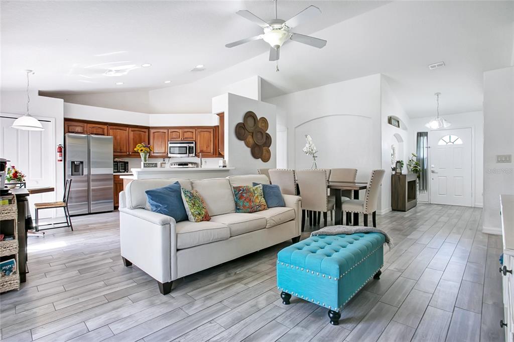 An open-concept living room features a white sofa, teal ottoman, and adjacent kitchen with wood cabinets — 4202 CRACKER COURT, ST CLOUD, FL