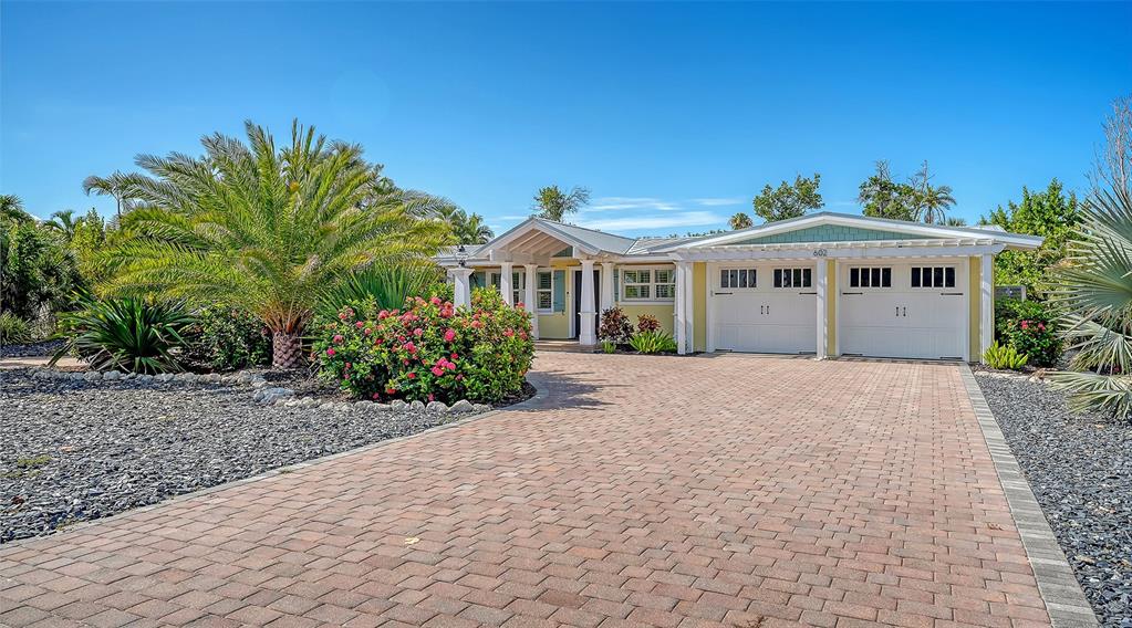 A single-story house with a white garage and a brick driveway surrounded by tropical landscaping — 602 BUTTONWOOD DRIVE, LONGBOAT KEY, FL