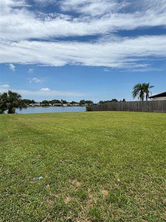 A grassy vacant lot overlooks a lake with a wooden fence on the right side — 4368 SUNRAY DRIVE, HOLIDAY, FL