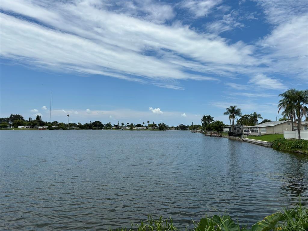 A view of a lake with houses along the shore under a cloudy blue sky — 4368 SUNRAY DRIVE, HOLIDAY, FL