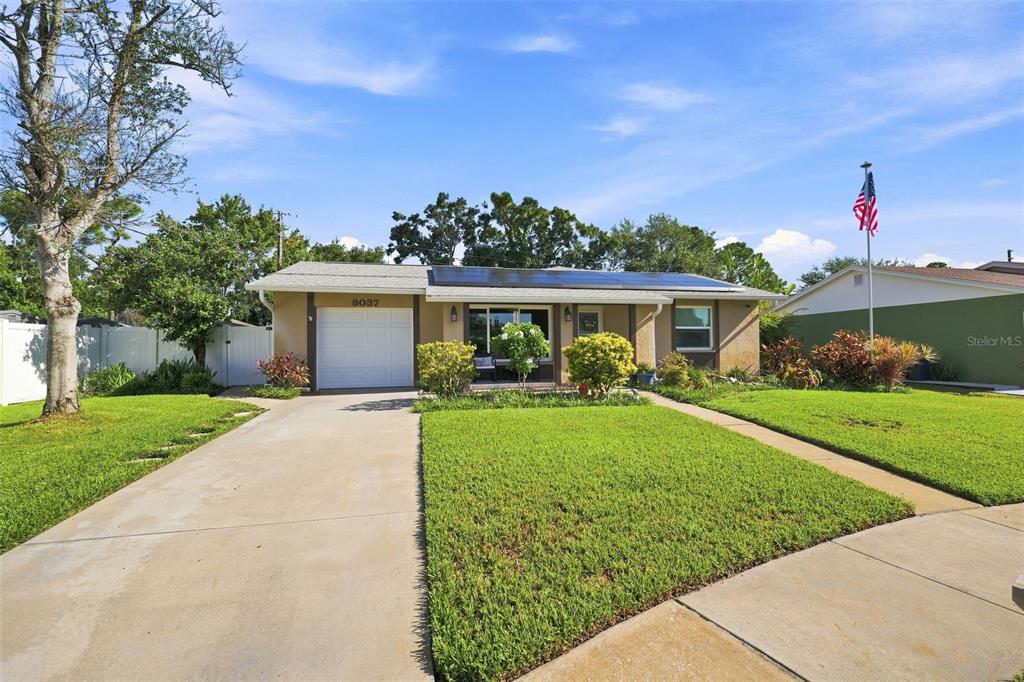 A single-story house with a concrete driveway, a garage, and solar panels on the roof — 8037 POWDER HORN CIRCLE, LARGO, FL