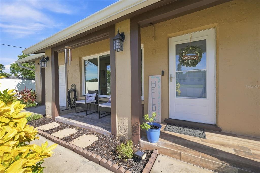 A covered porch features a white front door, a welcome sign, and outdoor seating — 8037 POWDER HORN CIRCLE, LARGO, FL